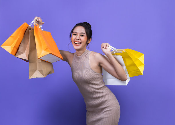 亚洲年轻漂亮的女人正在用智能手机网上购物，购物袋孤立在紫罗兰色的背景与复制空间。图片下载