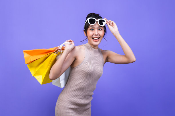 亚洲年轻漂亮的女人正在用智能手机网上购物，购物袋孤立在紫罗兰色的背景与复制空间。图片下载