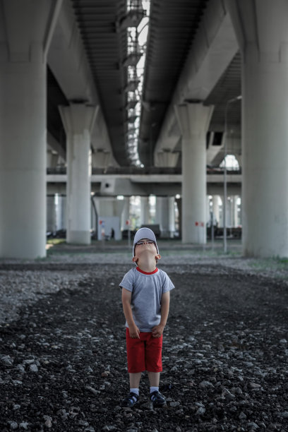 小男孩抬头站在高速公路立交桥下——迷失在大都市，都市童年在大城市图片下载