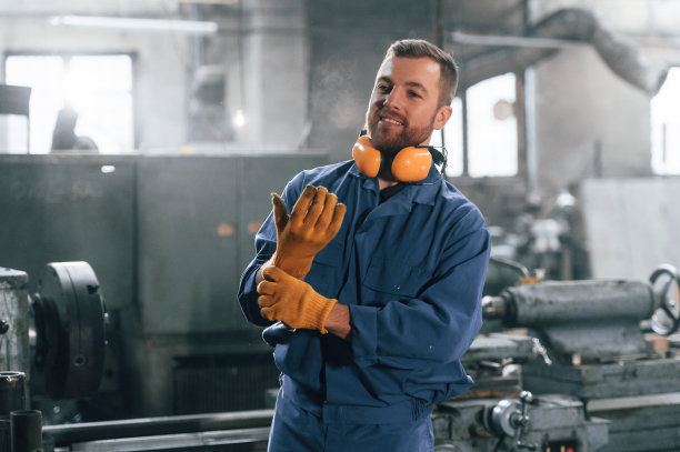 戴着手套和防护耳机。穿蓝色制服的工厂工人在室内图片下载