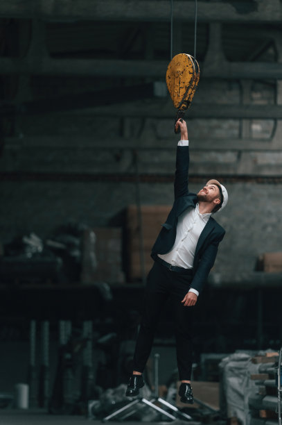 吊在吊车钩上。身着黑色正装的经理在工厂图片下载