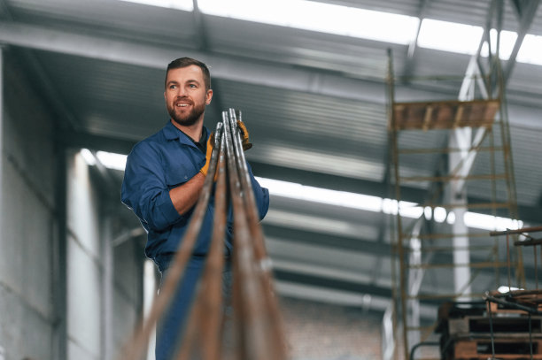 拿着金属管。穿蓝色制服的工厂工人在室内图片下载