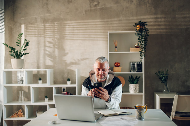 中年男子在家庭办公室工作时使用智能手机和笔记本电脑图片下载