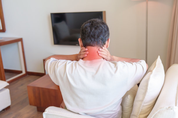 一名男子坐在沙发上脖子和肩膀疼痛。由于纤维肌痛，风湿，肩胛骨痛，办公室综合症和人体工程学的概念图片下载