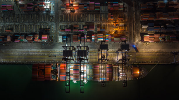 鸟瞰图国际航运港口装卸集装箱的起重机上的运输船和拖车进出口分发产品给客户和消费者在夜景照明图片下载