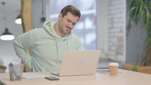 年轻男子使用笔记本电脑时背部疼痛图片下载