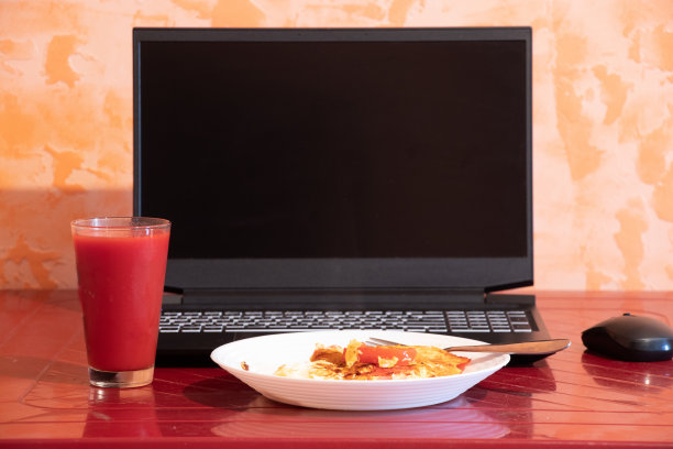 炒鸡蛋配一杯番茄汁放在红桌子上，他们拿了一台黑色笔记本电脑在家里的厨房里，一边工作一边有一台笔记本电脑图片下载