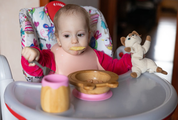 婴儿吃的是儿童用的木制餐具。图片下载