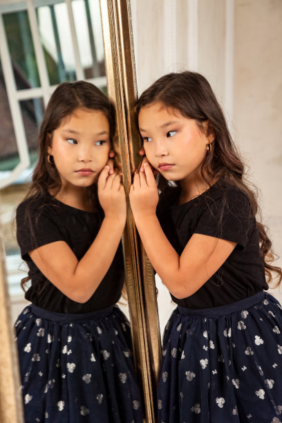 亚洲小孩时装模特在镜子室内摆姿势，看反射。肖像时尚的年轻女士孩子女孩女演员在客厅。时尚的风格理念。复制广告的文字空间图片下载