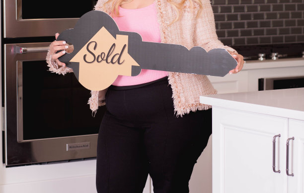 特写镜头是一名身穿粉色夹克的女子在厨房里拿着一个写着“售出”的钥匙牌图片下载