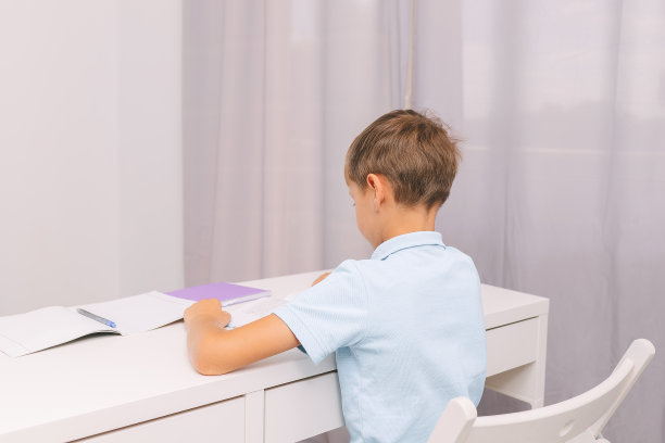 一个男孩坐在书桌前写字。从后面看。小学生。回到学校。图片下载