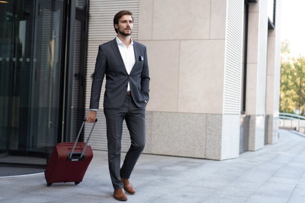 面带微笑，带着行李箱的经理走在现代化的办公室外面。图片下载