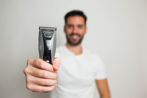 英俊的大胡子男子用修剪器修剪他的胡子图片下载