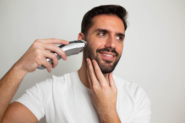 英俊的大胡子男子用修剪器修剪他的胡子图片下载