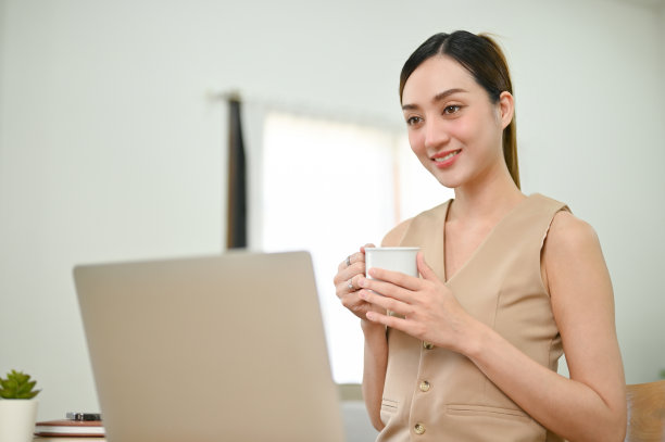 迷人的亚洲女商人拿着一杯咖啡，同时专注于她的笔记本电脑上的任务图片下载