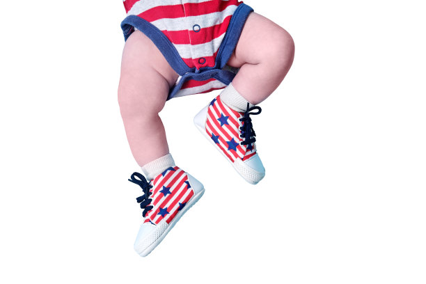 一个刚出生的婴儿鞋子上有美国国旗的颜色，孤立在白色背景上。一个穿着红白相间美国国旗靴子的孩子。两个月大的孩子图片下载