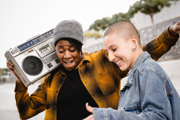 快乐的多种族的人们在户外随着城市音乐跳舞，背景是城市——来自不同文化的女性一起庆祝图片下载