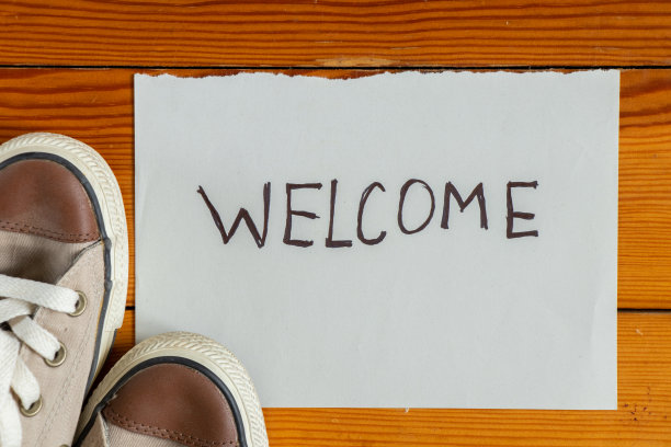 鞋子放在木地板上，旁边是一张写着“欢迎光临”的纸，鞋子放在房子的入口处图片下载