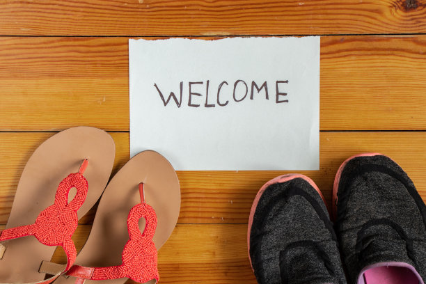 鞋子放在木地板上，旁边是一张写着“欢迎光临”的纸，鞋子放在房子的入口处图片下载