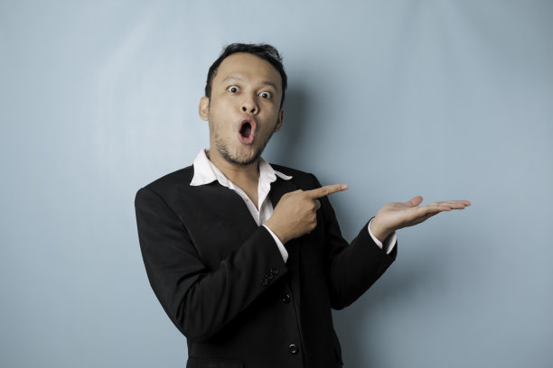 穿着西装的亚洲男人惊讶地指着他旁边的复印空间，微笑着，被蓝色的背景隔离图片下载