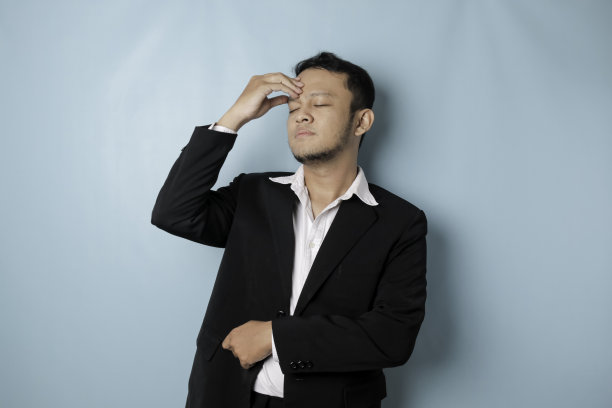 亚洲商人看起来疲惫沮丧，抱着头露出悲伤的表情。孤立的蓝色背景图片下载