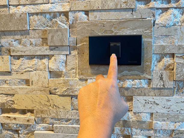 女人的手指和手按黑色电动开关打开或关闭与粗糙纹理的花岗花砖图案的墙壁背景图片下载