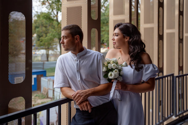 一对热恋中的情侣站在停车场的栏杆旁。一对可爱的白人夫妇站在停车场，从高处俯瞰这座城市。城市风格的婚礼。图片下载
