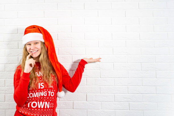 正面的照片女孩戴着圣诞老人的帽子手示范圣诞新年促销促销摸牙齿手指穿暖和的冬天的衣服图片下载