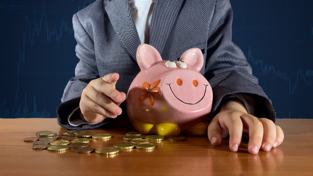 穿西装的孩子在储蓄罐旁边指着手指。背景为股票市场图表。理财教育，为孩子储蓄的概念图片下载