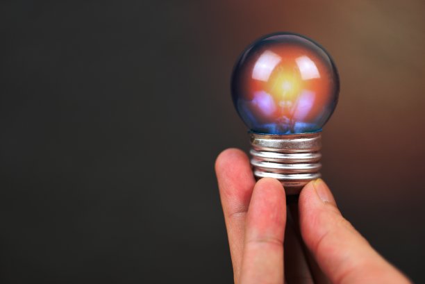 手持灯泡，黑色背景灯发出的光-节能理念，节电和世界理念图片下载