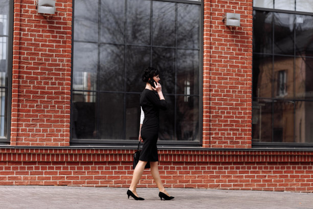 快乐的律师、女商人、职业人士正在户外用智能手机聊天。白人成功女性微笑着穿着时髦的黑白连衣裙和黑色包图片下载