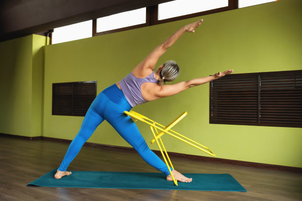 一名生活方式健康的女性正在练习瑜伽，在椅子上做三角式运动，穿着运动服在健身中心训练图片下载