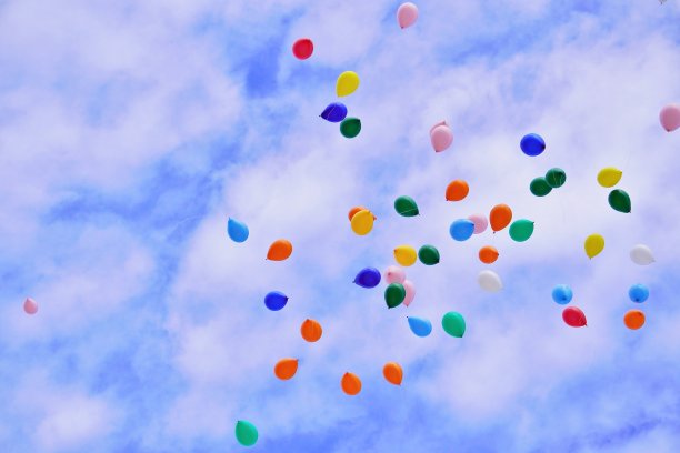 大量的彩色气球在蓝天上放飞，伴着薄薄的白云图片下载
