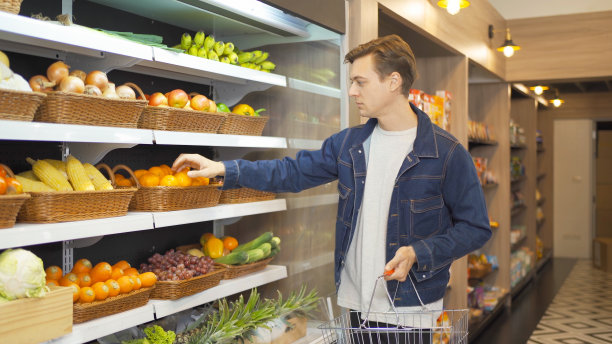 一名白人男性顾客正走在超市的货架上，拿着购物篮购买水果和蔬菜。购买食物。人们的生活方式。图片下载