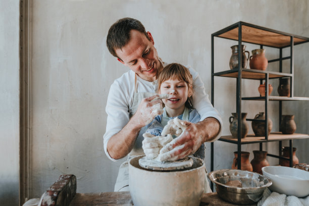 一个年轻的男人和他的女儿在制陶轮上摆弄陶土图片下载