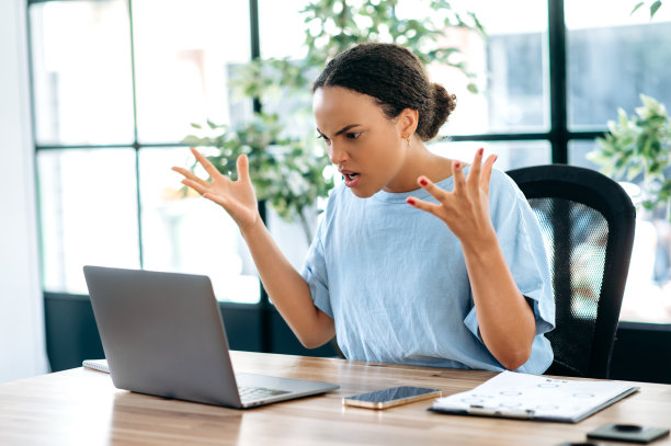 愤怒的年轻的混血商业女士，公司董事，监事，坐在办公室里看着笔记本电脑屏幕，用手比划，对员工表现不佳感到恼火图片下载