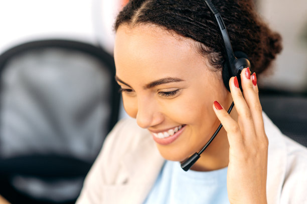 正面混血儿卷发女子特写照片，戴着耳机，呼叫中心座席，支持服务操作员，坐在办公室，在线咨询客户，倾听信息，微笑友好图片下载