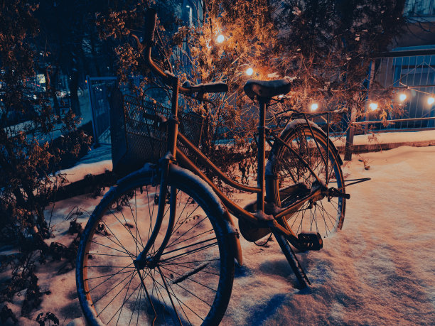 被遗忘在雪地里的自行车和温暖的灯光。夜晚精选照片复古冬季背景。图片下载