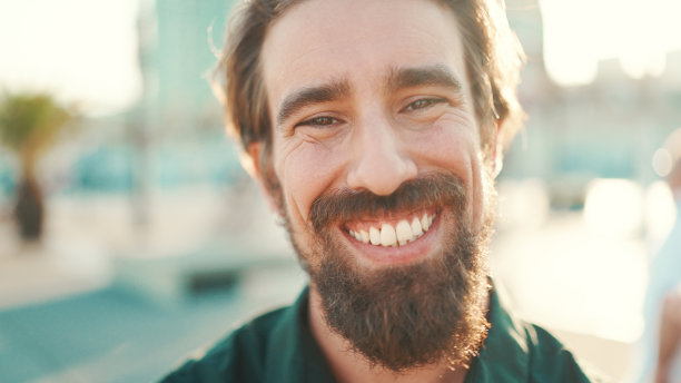 特写肖像的微笑男子与胡子在城市的背景。正面特写的快乐年轻潮人男性看着相机图片下载