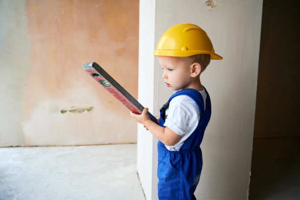 小男孩建筑工人用水平仪检查墙壁。图片下载