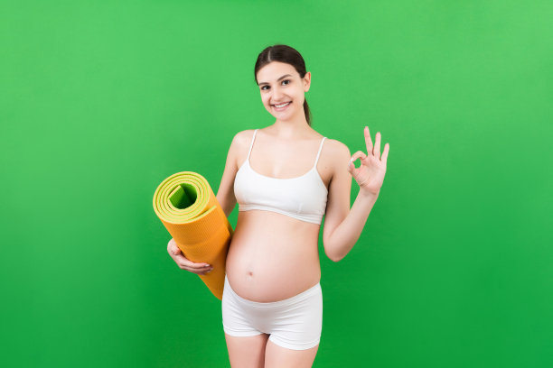 怀孕的女孩抱着瑜伽垫站在彩色背景。工作室拍摄，自由空间的设计图片下载