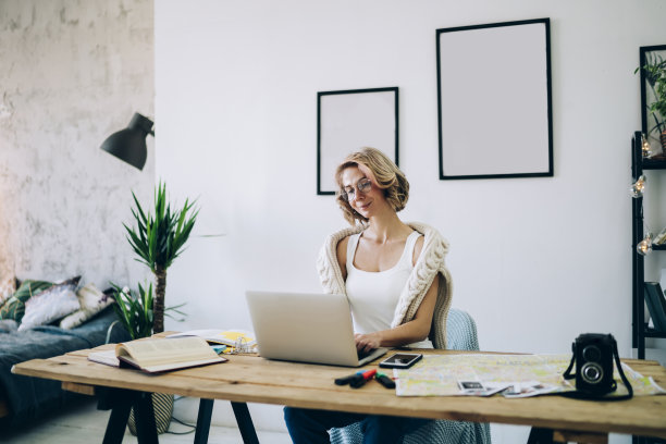 年轻微笑的女人坐在舒适的工作场所，在现代笔记本电脑上使用高速家庭互联网在网络上阅读新闻，方便远程自由工作的概念图片下载