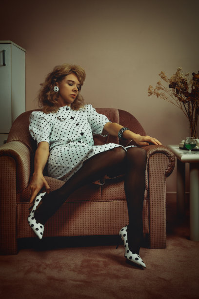 一个80年代末、90年代初的年轻金发女子的复古生活方式画像，室内装饰，穿着黑白圆点服装，坐在粉红色的沙发上，脱下鞋子图片下载