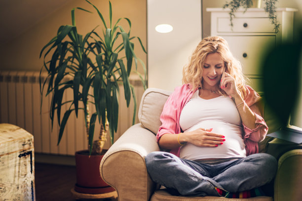 美丽的孕妇坐在家里的椅子上使用智能手机图片下载