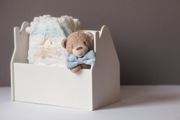 木制玩具，一只戴领结的熊，一堆尿布，一个奶瓶和婴儿用品放在换尿布的桌子上。文本空格。图片下载