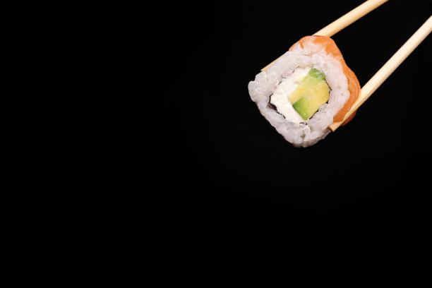 寿司，三文鱼和鳄梨卷的特写，用筷子夹在黑色背景上。文本复制空间图片下载
