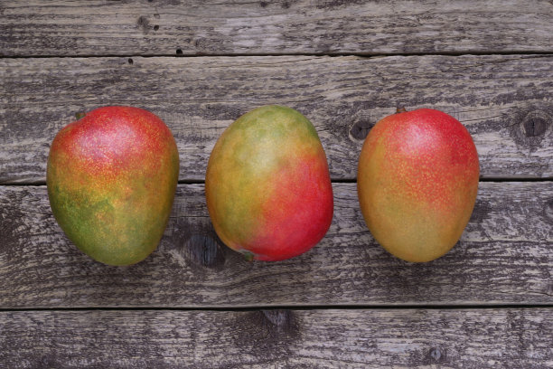 木制背景上的芒果水果，桌面视图。三个完整的成熟芒果排在深色木板上，从上面直接拍摄。图片下载