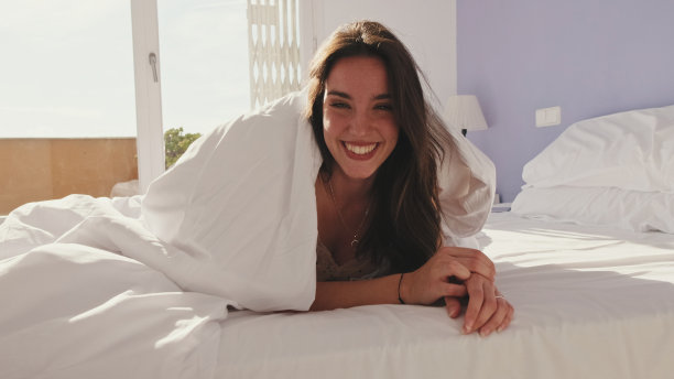 特写，快乐的女孩在床上摆姿势。一个笑着的女孩从毯子下面探出头来图片下载