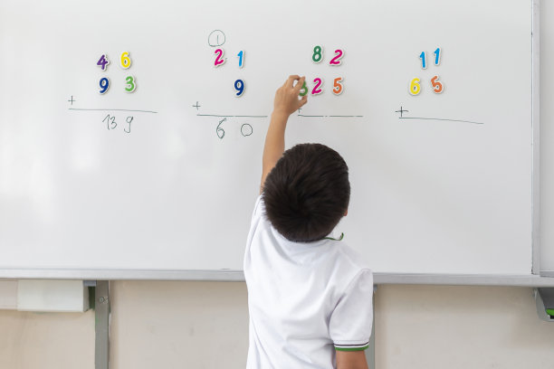 小学生穿着校服在白板上用磁性数字解题。图片下载