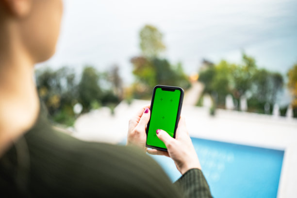 年轻的女孩使用手机与绿色屏幕在海边的阳台上的股票照片图片下载